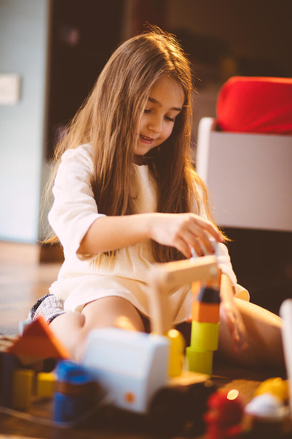 Young blond girl playing with toy blocks on the floor Photograph by Wundervisuals