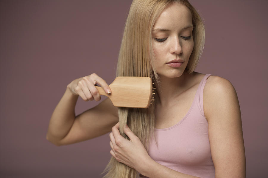 Young blonde woman brushing her hair, close-up Photograph by Stock4b-rf