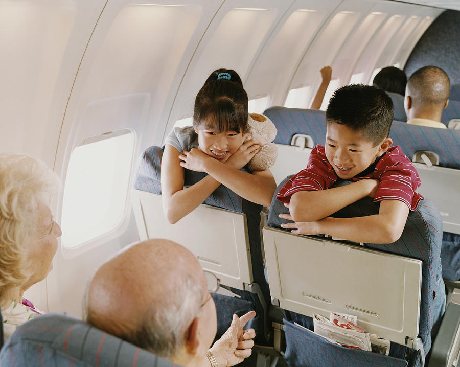 Young Boy and Girl Sit on a Plane, Talking to a Senior Couple Behind Them Photograph by Digital Vision.