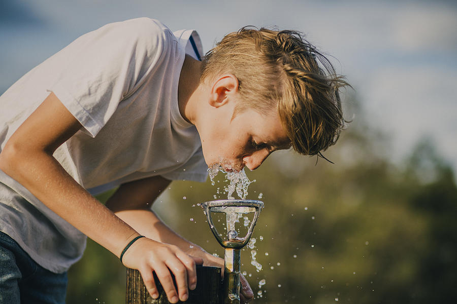 Young Boy Drinking from a Water Fountain Photograph by SolStock