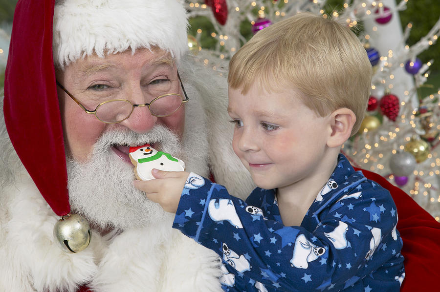 Young Boy in Pyjamas Feeds Father Christmas a Snowman Cookie Photograph by Digital Vision.