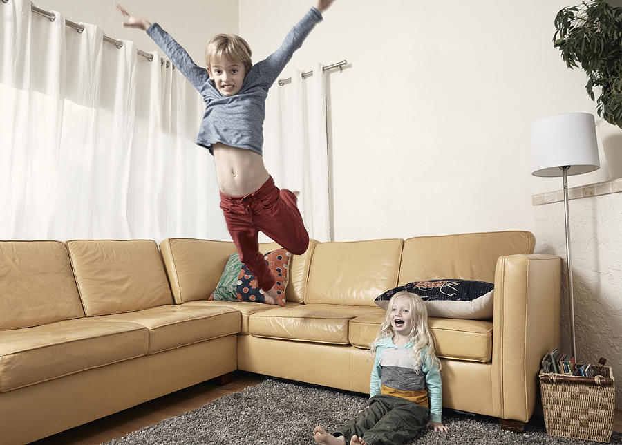 Young boy jumping off couch with little brother. Photograph by Troy Aossey
