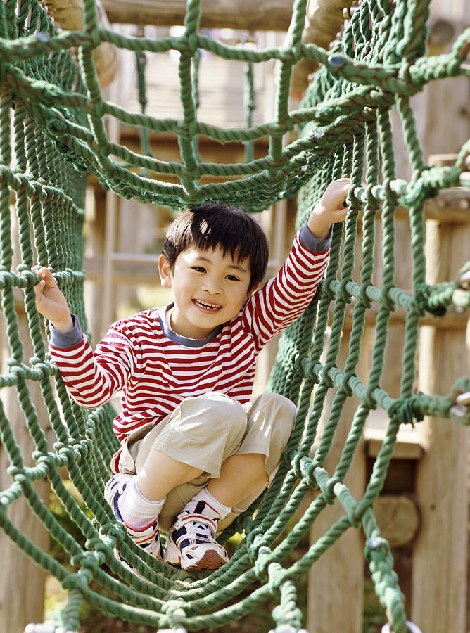 Young Boy Playing on Climbing Ropes in an Adventure Playground Photograph by Digital Vision.
