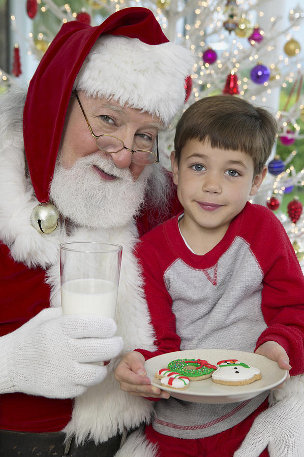 Young Boy Sits on Father Christmas Lap With a Plate of Cookies and a Glass of Milk Photograph by Digital Vision.
