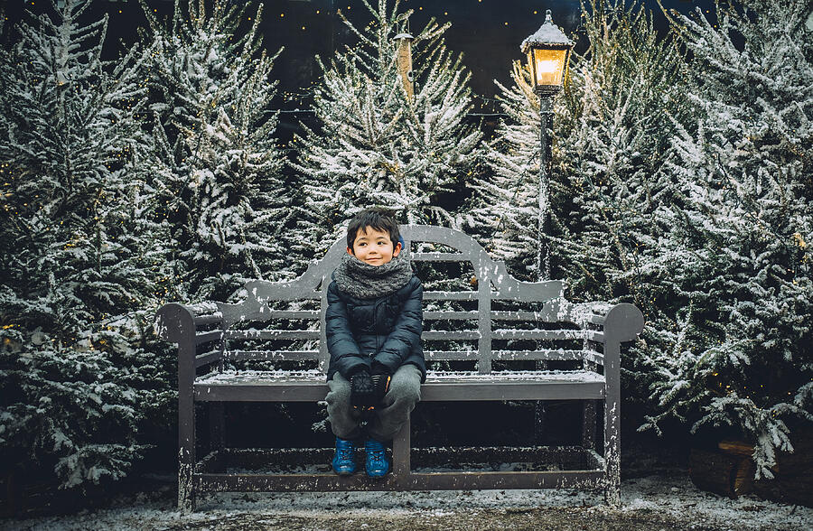 Young boy sitting on a bench in a festive Christmas setting. Photograph by © Peter Lourenco