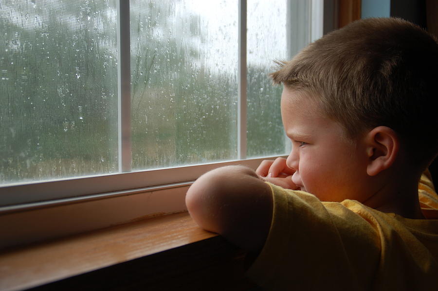 Young boy staring out a window as it rains Photograph by Kkay