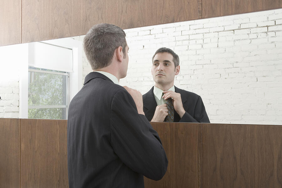 Young businessman adjusting tie in mirror Photograph by Charlie Schuck
