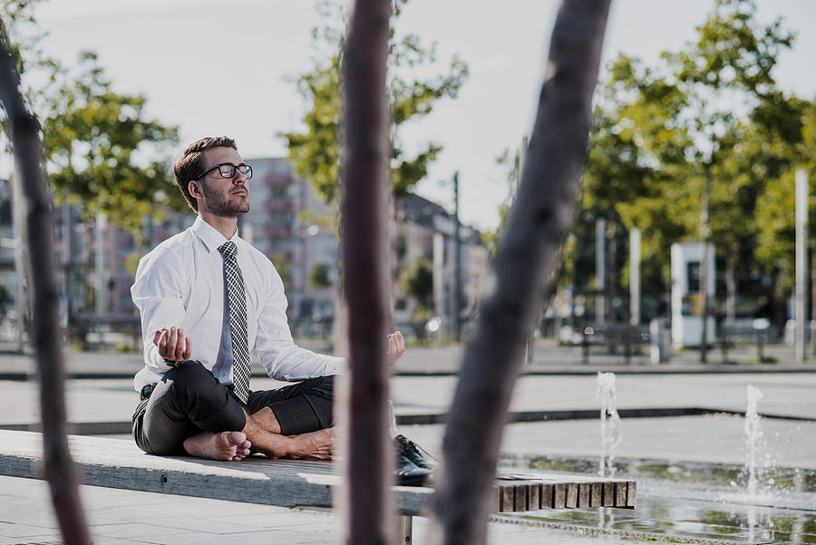 Young businessman meditating on bench Photograph by Westend61