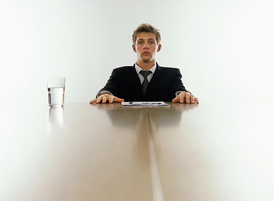 Young businessman sitting at end of table, portrait Photograph by Peter Cade