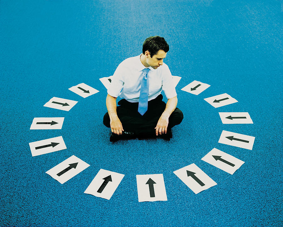 Young Businessman Sitting Cross Legged on the Carpet Inside a Circle of Arrow Signs Pointing Inwards Photograph by Adam Gault