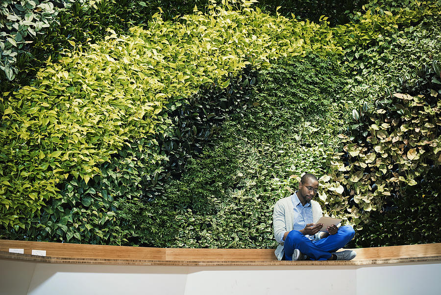 Young businessman using digital tablet in front of green plant wall Photograph by Westend61