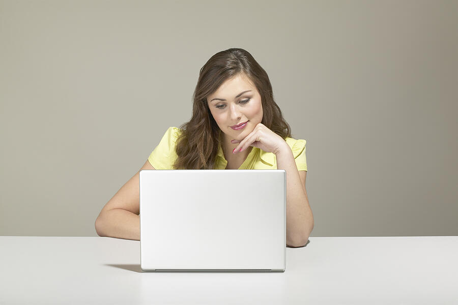 Young businesswoman sitting at desk using laptop Photograph by Richard Drury