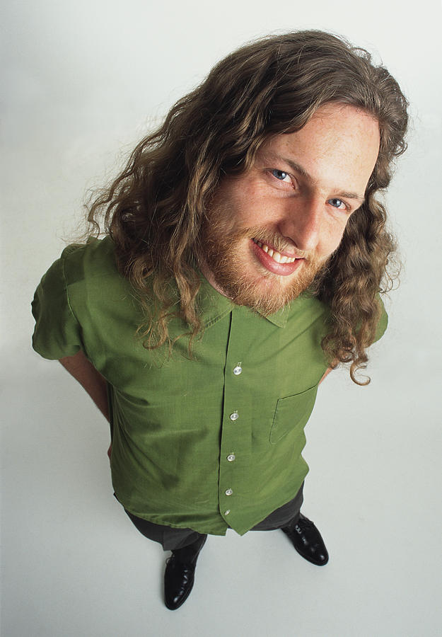 Young caucasian adult male hippie with facial hair and long curly hair wears a green shirt and stands looking up at the camera with a mischievous smile Photograph by Photodisc
