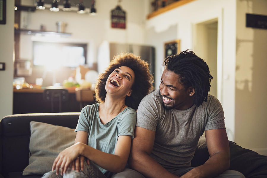 Young cheerful African American couple in the living room. Photograph by Skynesher