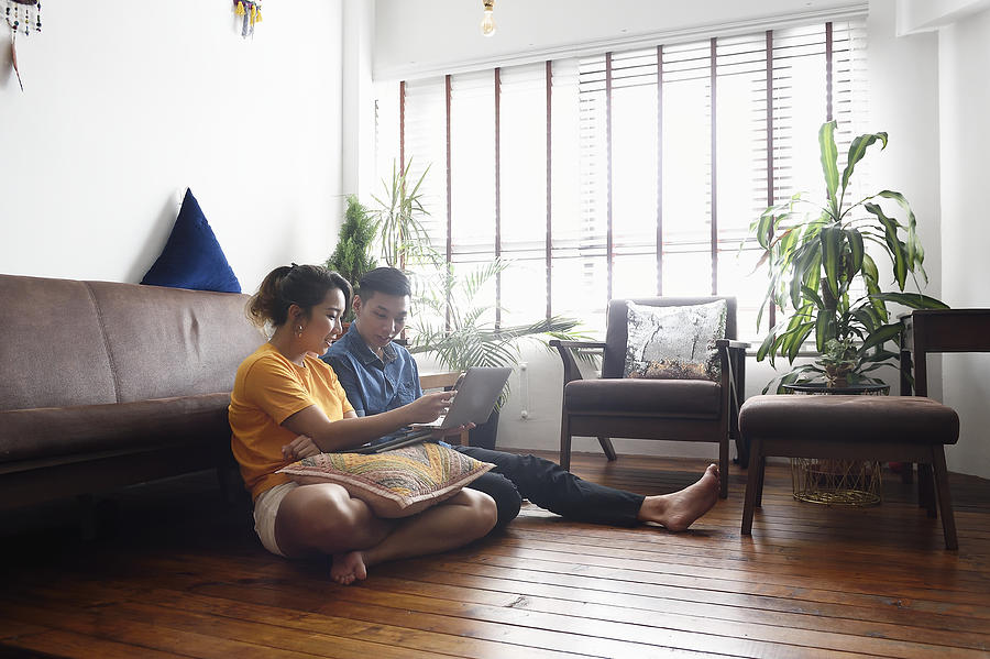 Young Chinese couple sitting on the floor at home with a laptop Photograph by Carlina Teteris