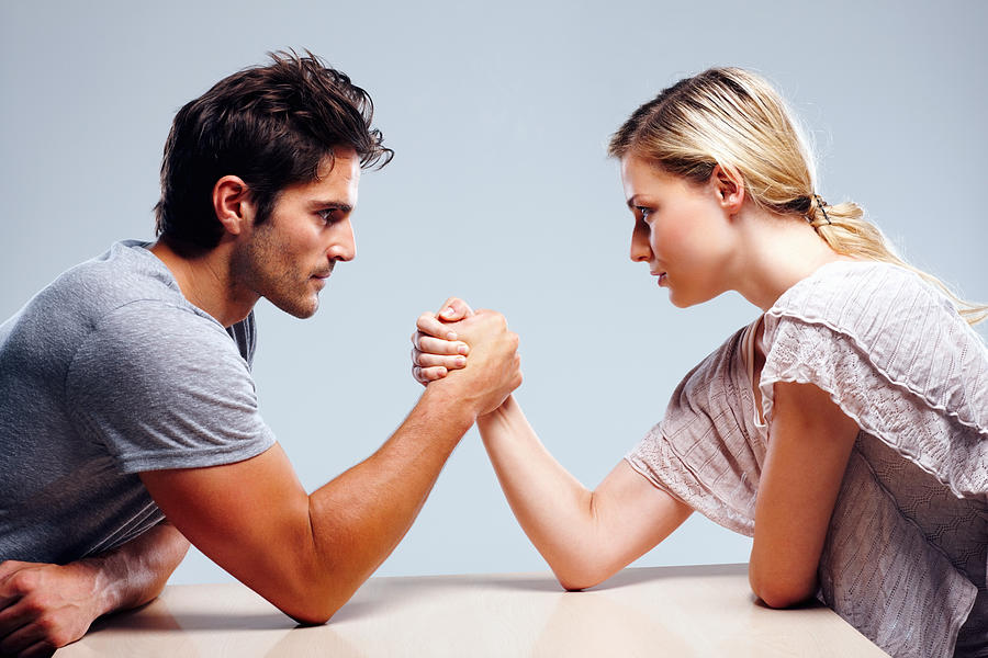 Young couple arm wrestling against grey background Photograph by Goodboy Picture Company