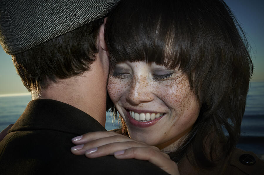 Young couple embracing on beach, smiling, close-up Photograph by Uwe Krejci