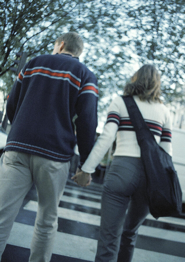 Young couple holding hands crossing on pedestrian crossing, rear view Photograph by Patrick Sheandell OCarroll