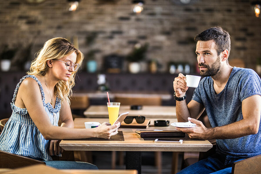 Young couple ignoring each other while sitting in a cafe. Photograph by Skynesher