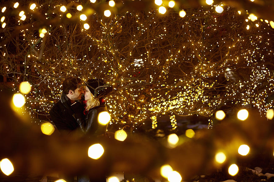 Young couple kissing surrounded by city xmas lights Photograph by Kevin Kozicki