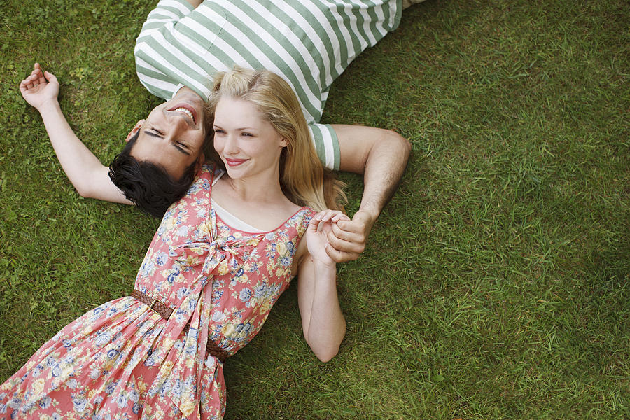 Young couple laying in grass and holding hands Photograph by Paul Bradbury