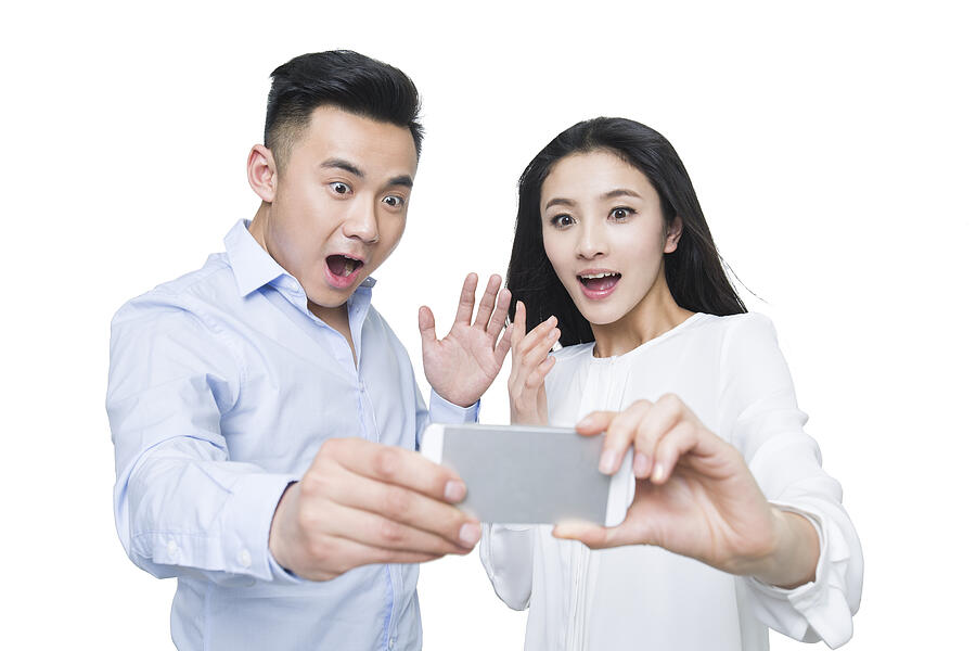 Young couple looking at smart phone with surprised expression Photograph by BJI / Blue Jean Images