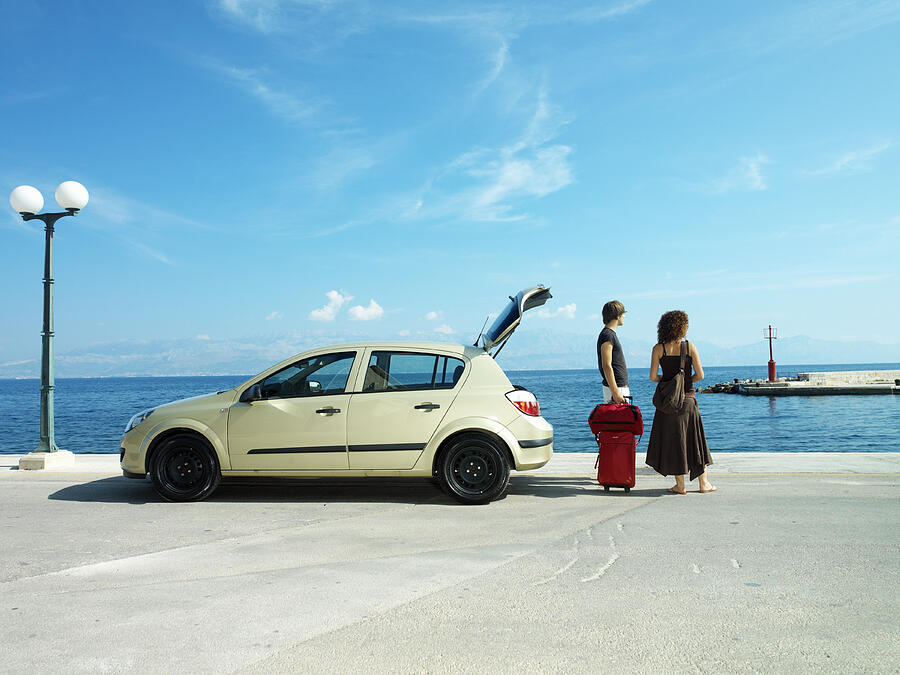 Young couple near car with luggage looking at ocean, rear view Photograph by Gary John Norman