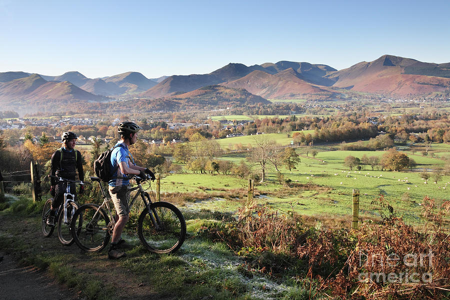 Young couple on bikes looking over Cumbrian fells, England, UK Photograph by Bryan Attewell
