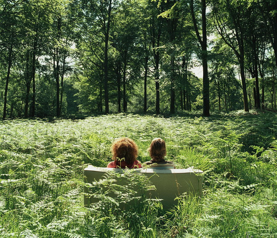 Young couple on sofa in forest glade, rear view Photograph by Martin Barraud