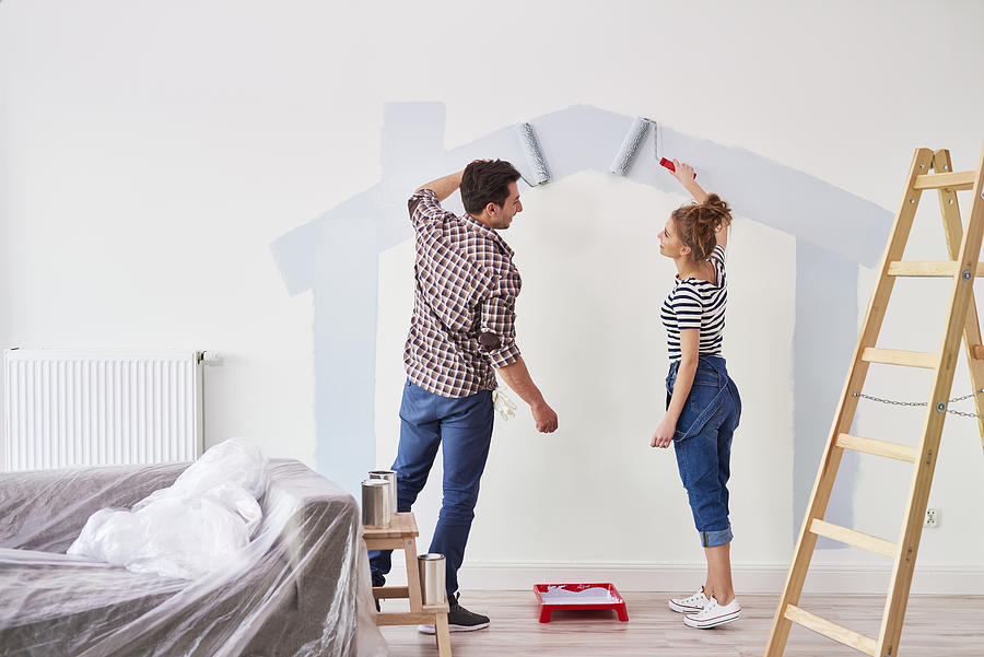 Young couple painting the interior wall in their new apartment Photograph by Gpointstudio