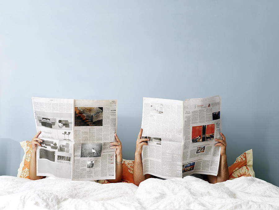 Young couple reading newspaper on bed Photograph by Jim Bastardo