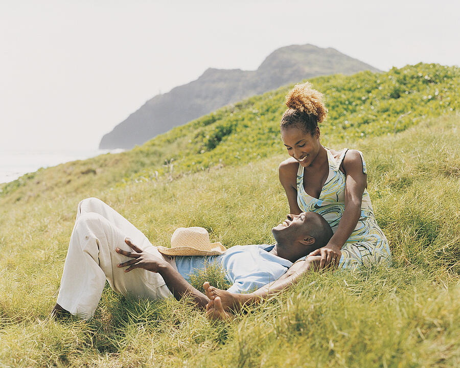 Young Couple Relax Looking at Each Other in the Grass of a Cliff top Photograph by Digital Vision.