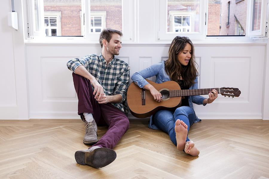 Young couple sitting on floor with woman playing guitar Photograph by Westend61