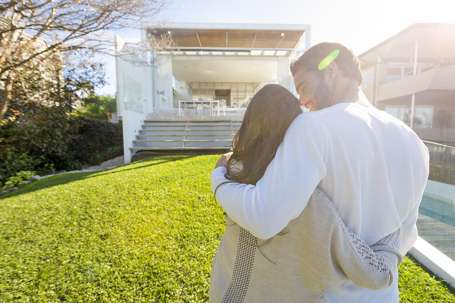 Young Couple standing in front of a modern new house. Photograph by Courtneyk