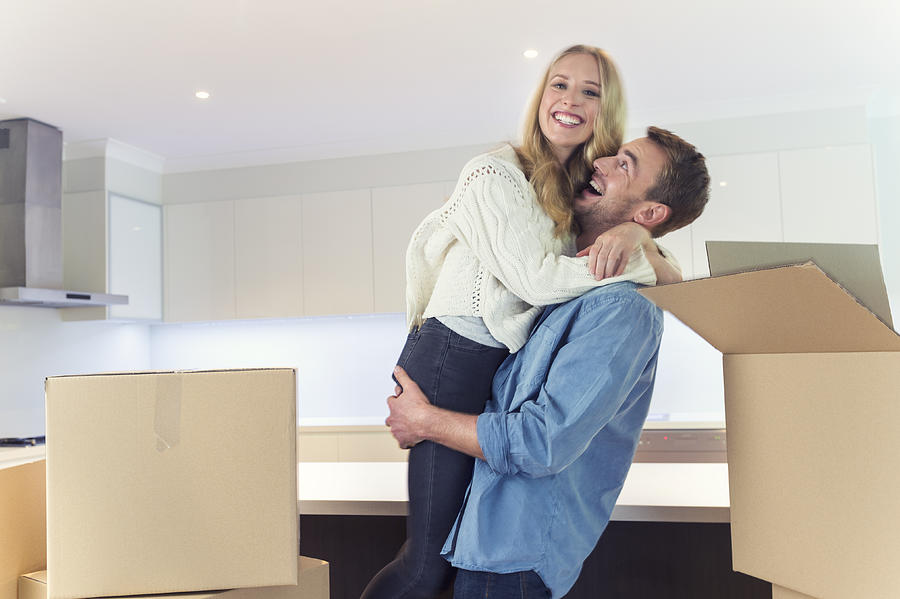 Young couple standing in new house with packing boxes. Photograph by Courtneyk