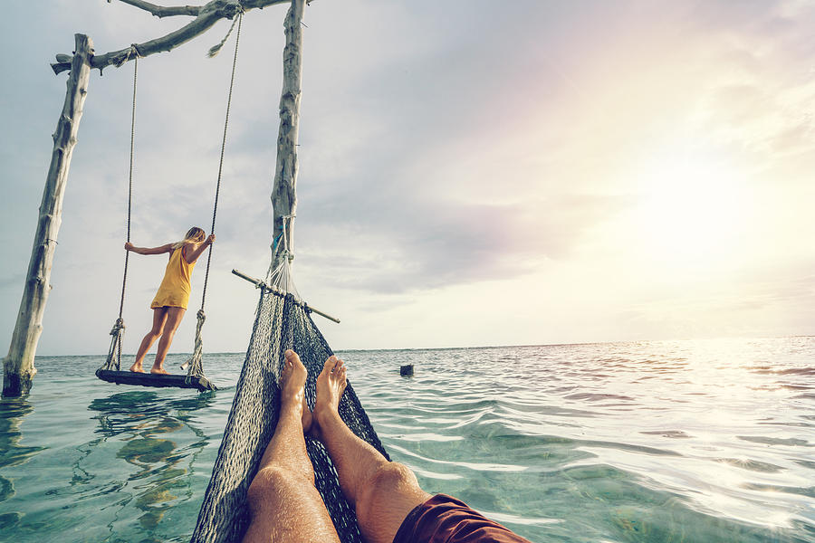 Young couple swinging on the beach by the sea, beautiful and idyllic landscape. People travel romance vacations concept. Personal perspective of man on sea hammock and girlfriend on sea swing. Photograph by Swissmediavision
