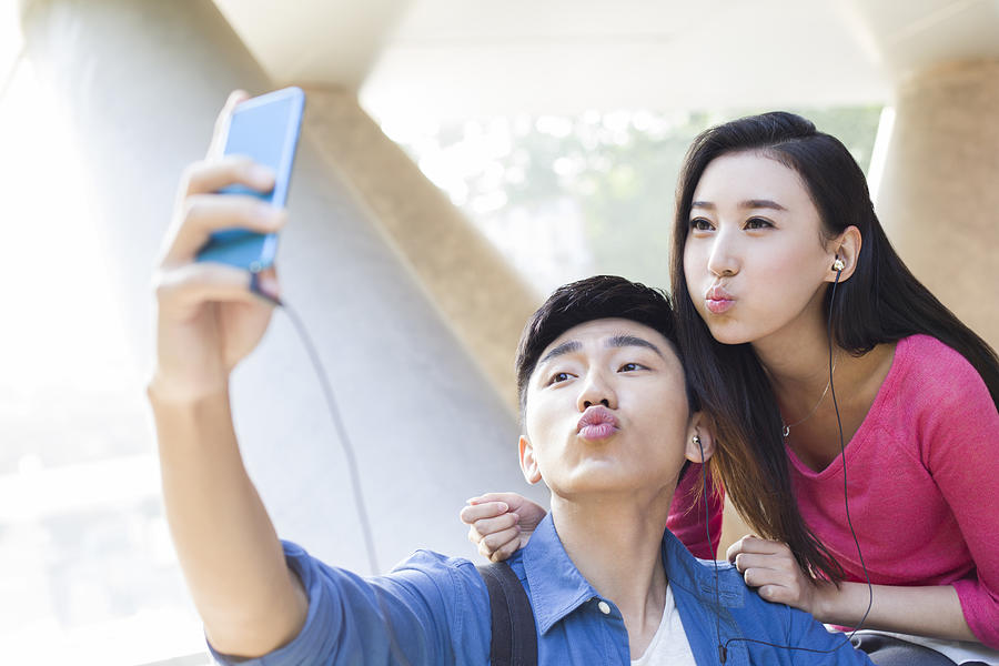 Young couple taking self portrait with a smart phone Photograph by Lane Oatey / Blue Jean Images