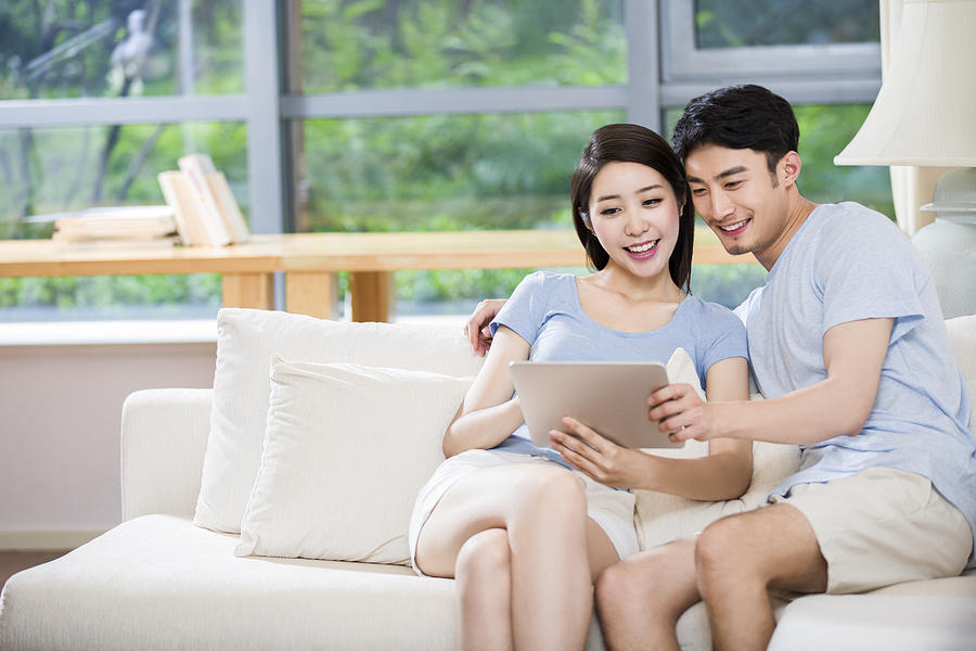 Young couple using digital tablet on sofa Photograph by BJI / Blue Jean Images
