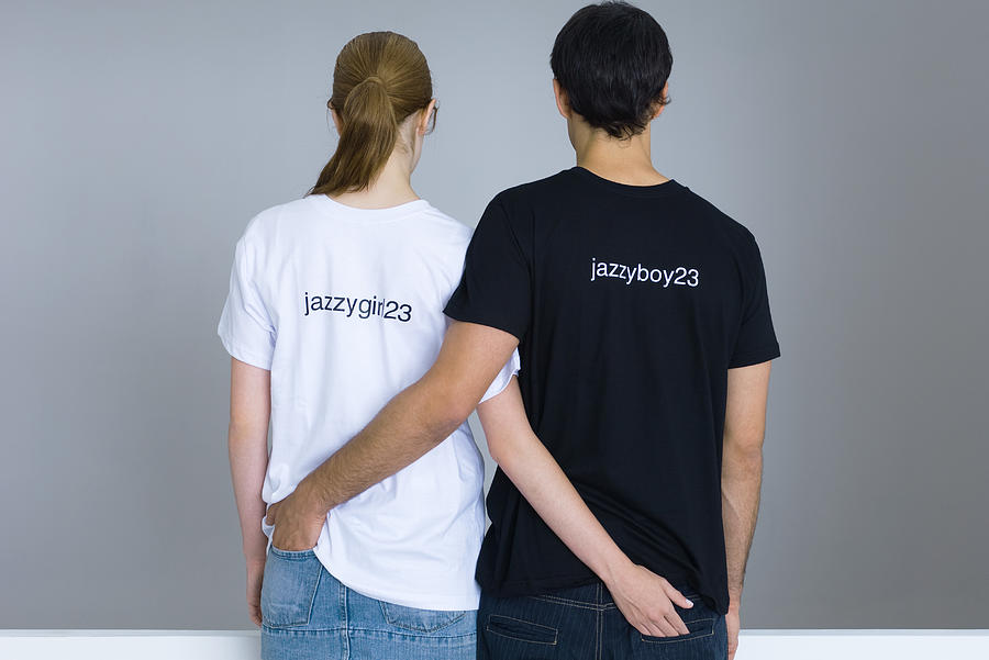 Young couple wearing customized tee-shirts, arms around each others waists, rear view Photograph by PhotoAlto/Michele Constantini
