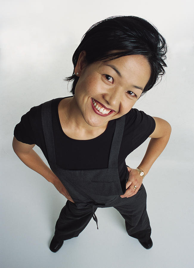 Young Cute Perky Asian Female Adult Wearing A Dark Jumper Looks Up At The Camera With Her Head To One Side While Flirting And Smiling Amusingly Photograph by Photodisc