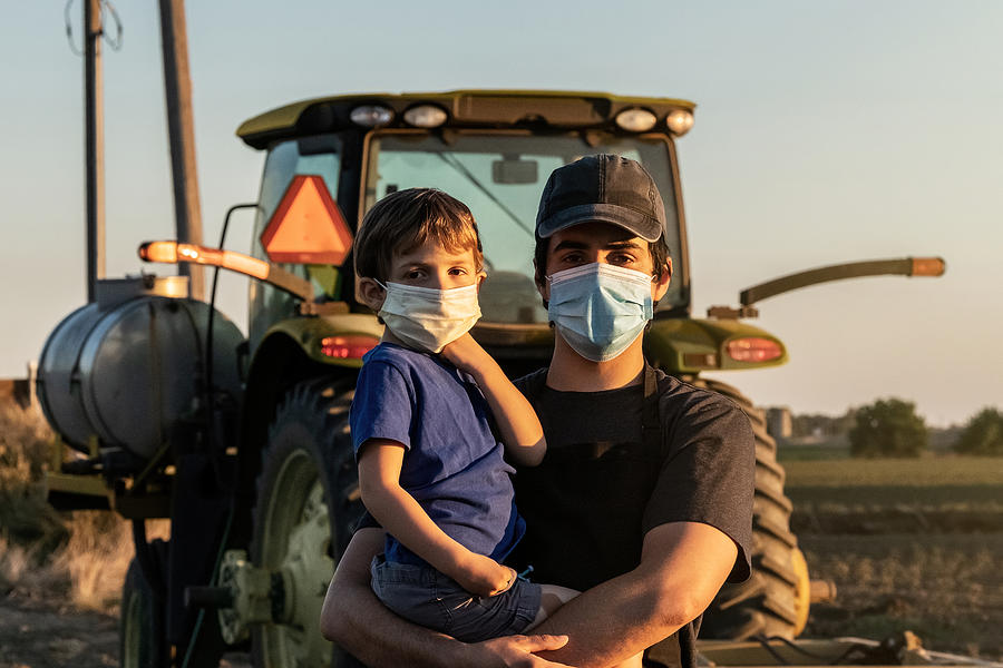 Young farmer posing with his son, both wearing protective face masks Photograph by Juanmonino