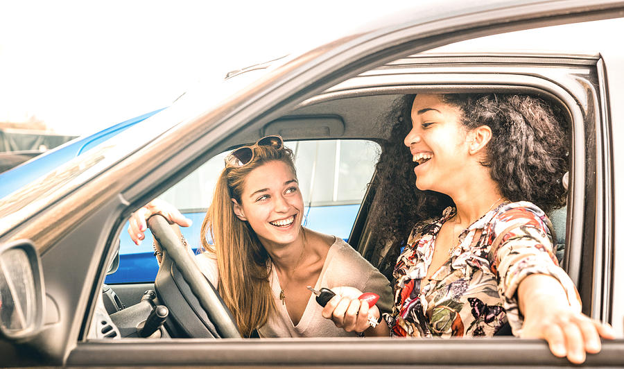 Young female best friends having fun at car roadtrip moment - Transportation concept and urban ordinary life with women girlfriends at happy travel vacation on the road - Bright azure filter Photograph by ViewApart