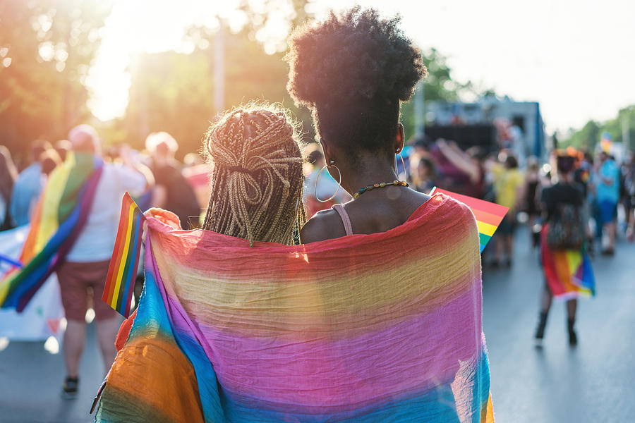 Young female couple hugging with rainbow scarf at the pride event Photograph by Mixmike