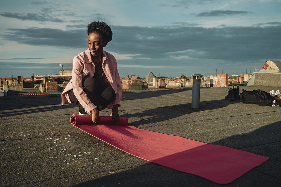 Young female folding exercise mat on rooftop during sunrise Photograph by Maskot