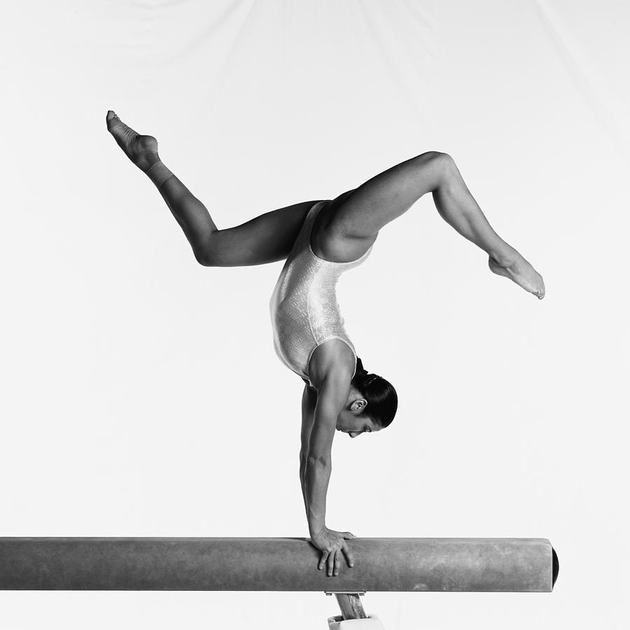 Young female gymnast on balance beam performing routine, side view, b&w. Photograph by Dominique Douieb