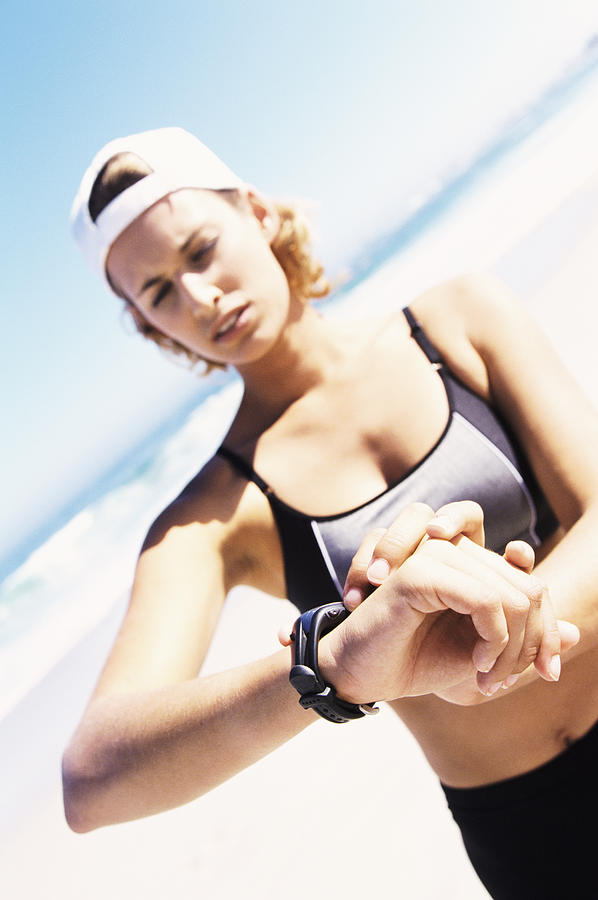 Young Female Jogger Checking the Time on Her Wristwatch Standing on a Beach Photograph by B2M Productions