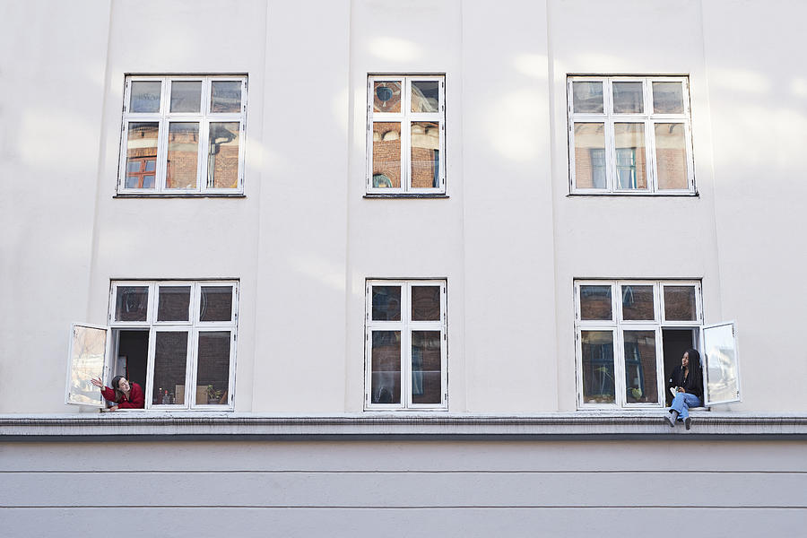 Young female neighbors talking from apartment windows Photograph by Klaus Vedfelt