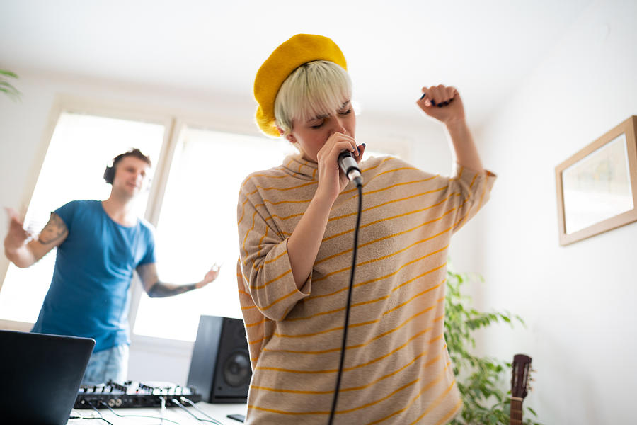 Young female rapper rapping while the dj plays the music in home music studio Photograph by SrdjanPav