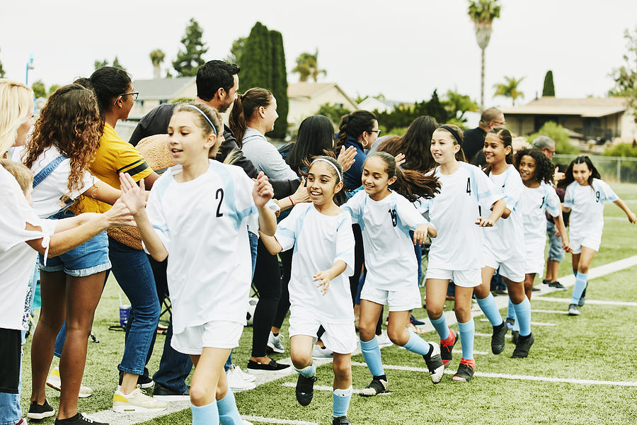 Young female soccer team giving high fives to parents on sidelines after game Photograph by Thomas Barwick