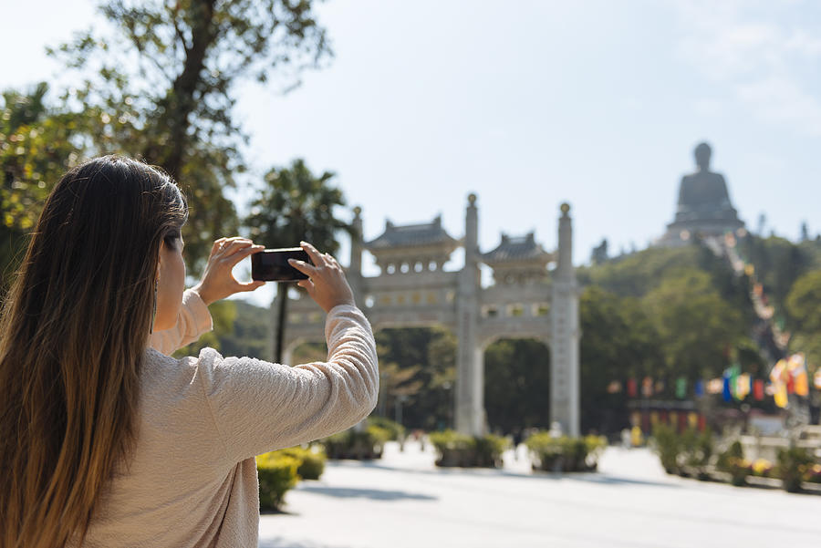 Young female tourist taking smartphone photographs of Tian Tan Buddha, Po Lin Monastery, Lantau Island, Hong Kong, China Photograph by Ben Pipe Photography